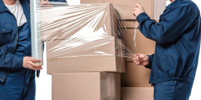 Two,Movers,Wrapping,Cardboard,Boxes,With,Roll,Of,Stretch,Film Two,Movers,Wrapping,Cardboard,Boxes,With,Roll,Of,Stretch,Film